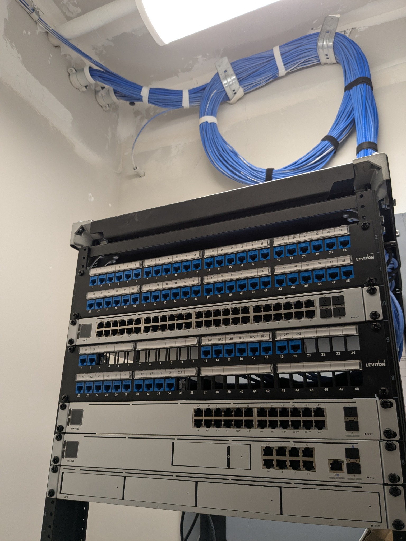 LVC cabling work in progress: blue cable runs, labeled patch panels and rack-mounted network equipment